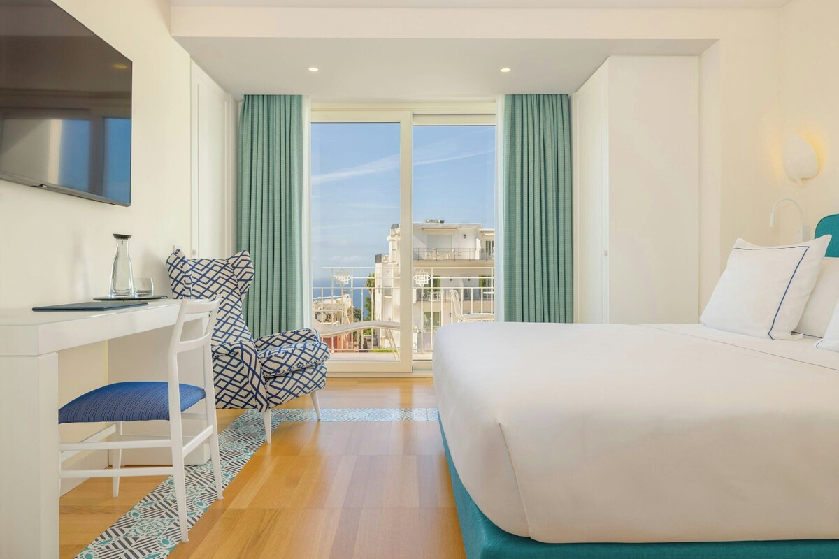 Een hotelkamer met een bed, een bureau, een stoel en uitzicht op buiten.