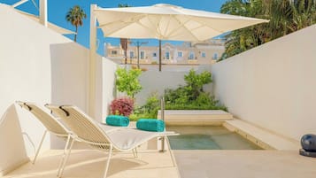Un área junto a la piscina con dos sillones de descanso, una sombrilla blanca y una piscina pequeña.