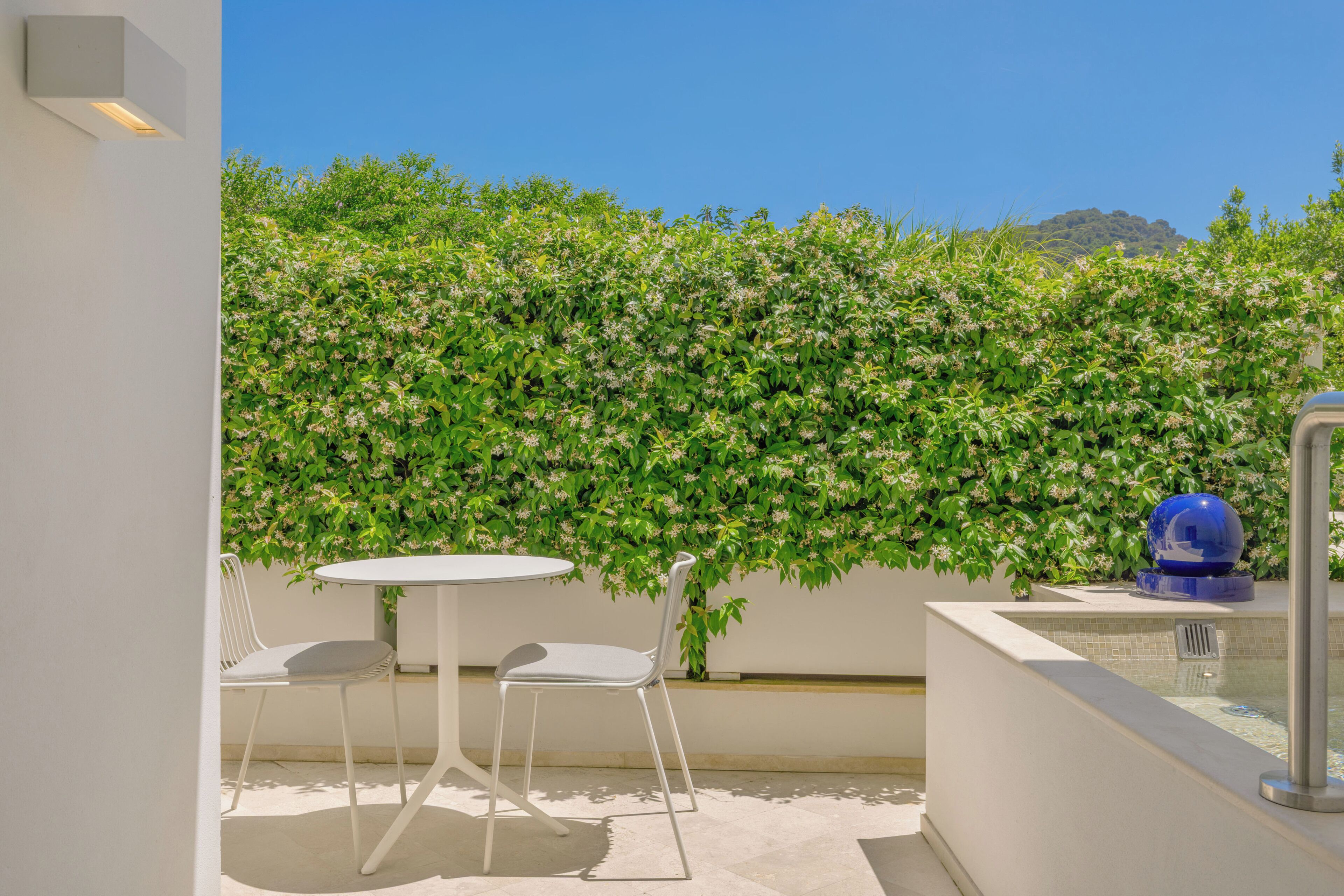 Un balcon avec une table blanche et deux chaises, un objet décoratif bleu et un mur végétal vert.