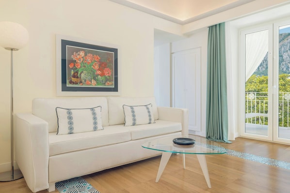 Una sala de estar moderna con un sofá, una mesa de centro de vidrio, una obra de arte enmarcada y vistas a través de un ventanal.