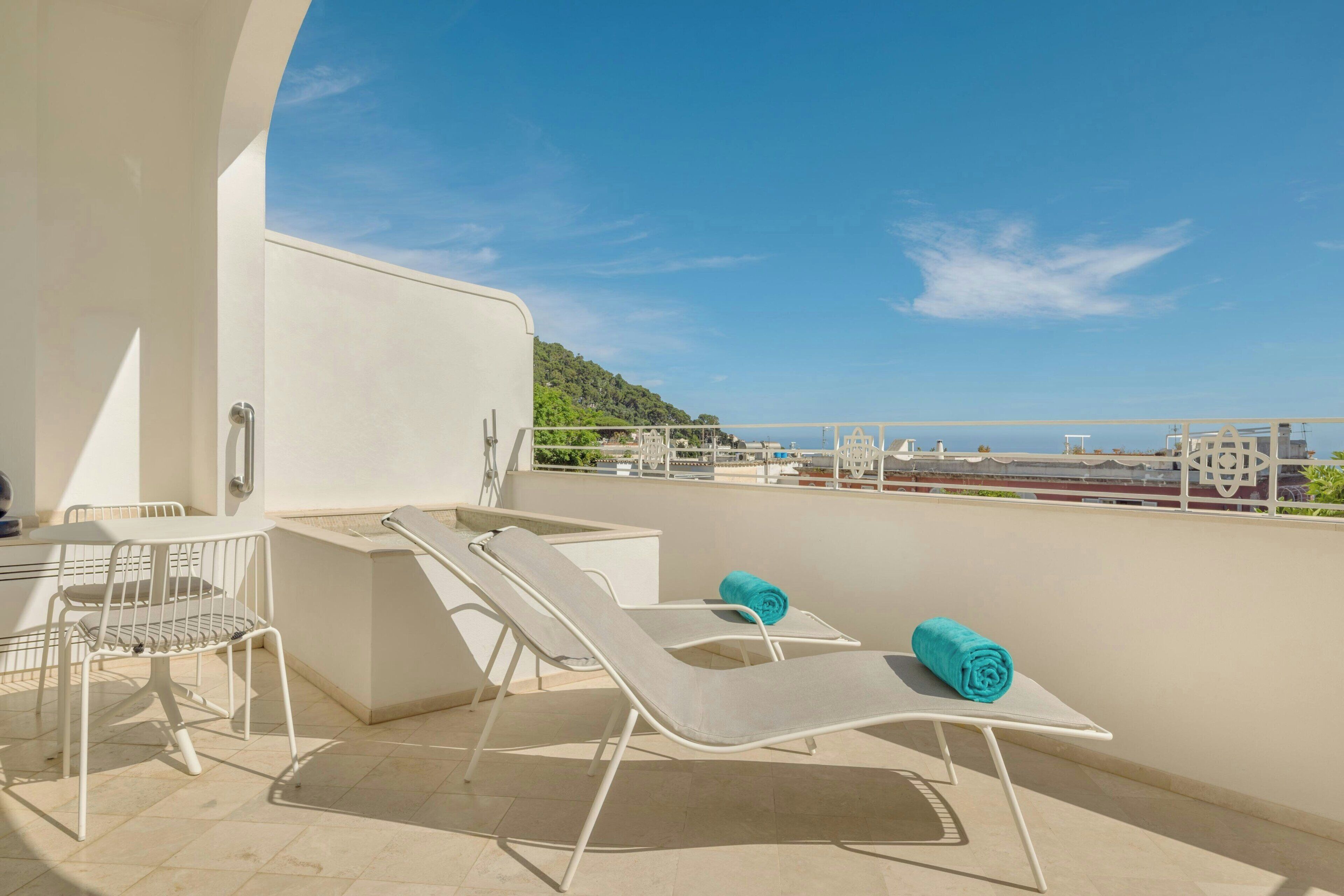 A balcony with a pool table, two lounge chairs, and a view of the sea.