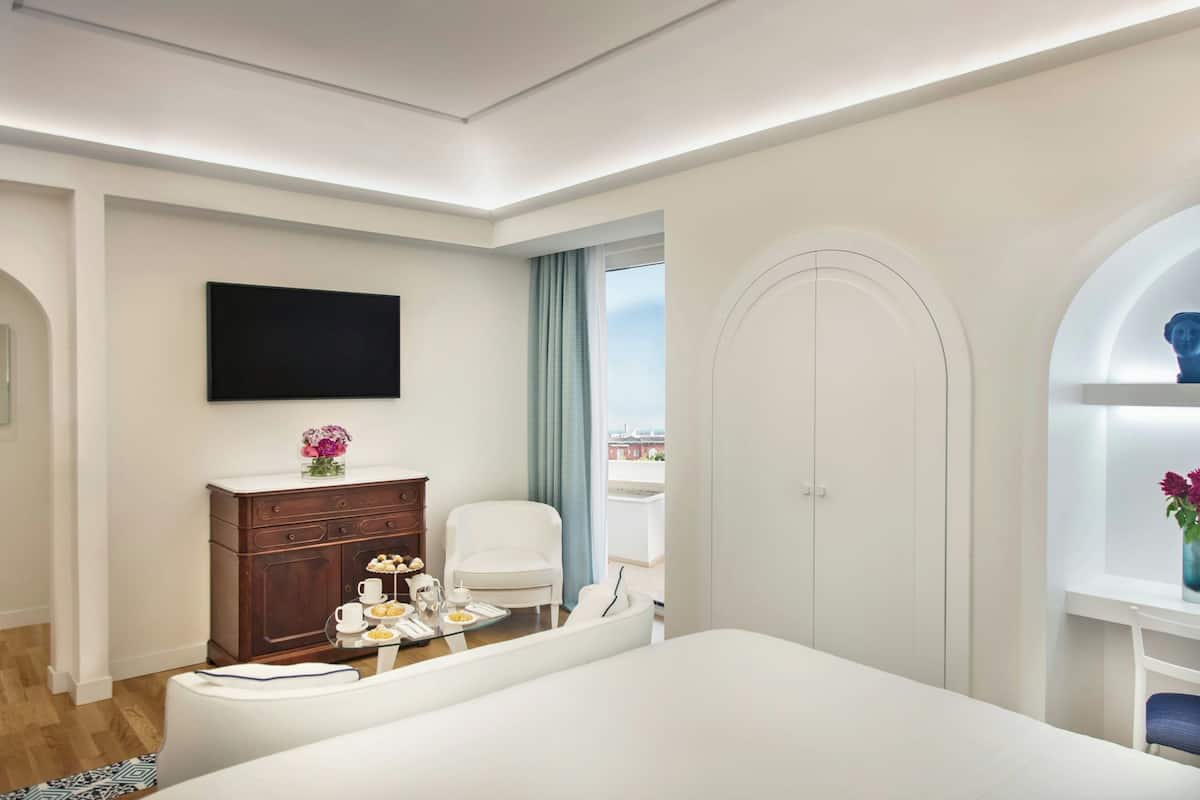 Une chambre d’hôtel moderne dotée d’un grand lit, d’un téléviseur à écran plat, d’une commode en bois, d’une table à manger agrémentée d’un vase de fleurs et offrant une vue sur la ville grâce à une grande fenêtre.