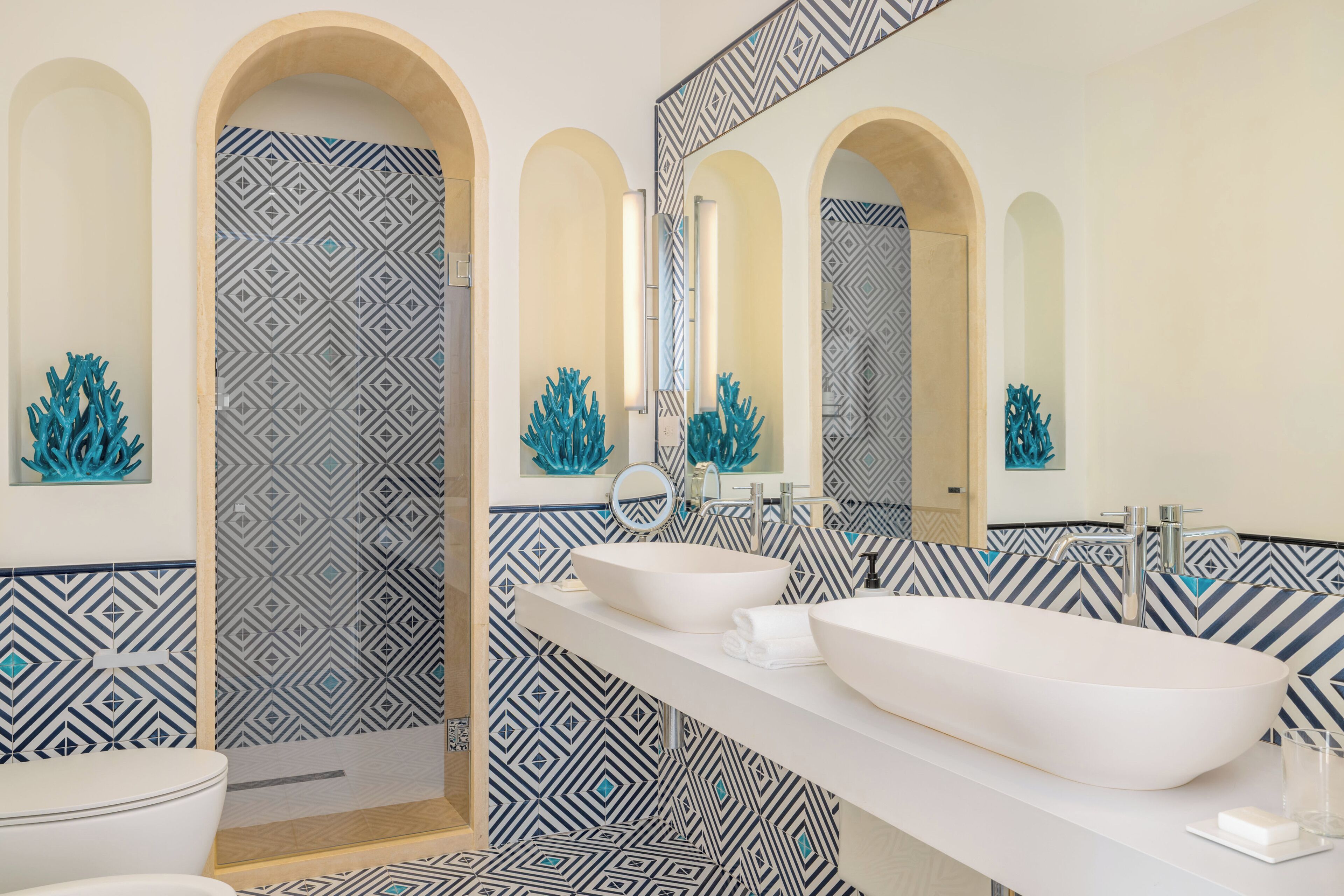 A modern bathroom with two sinks, a mirror, and decorative coral sculptures.