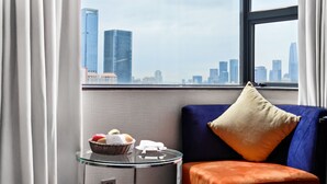 A room with a city view, a glass table with fruits, a blue sofa with an orange cushion, and a white wall. - The Pavilion Century Tower Hotel (Shenzhen)