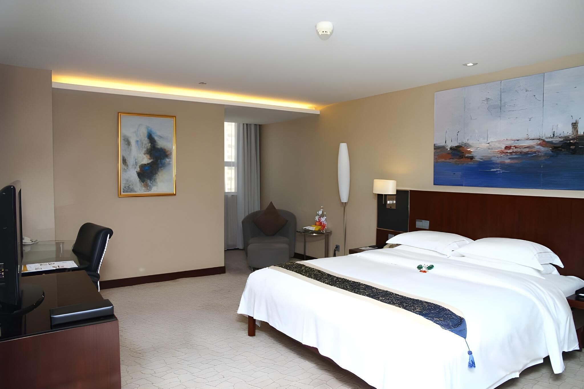 A hotel room with a bed, desk, chair, and artwork on the walls.