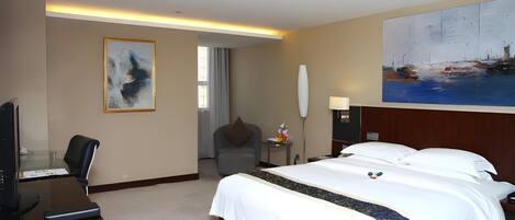 A hotel room with a bed, desk, chair, and artwork on the walls.