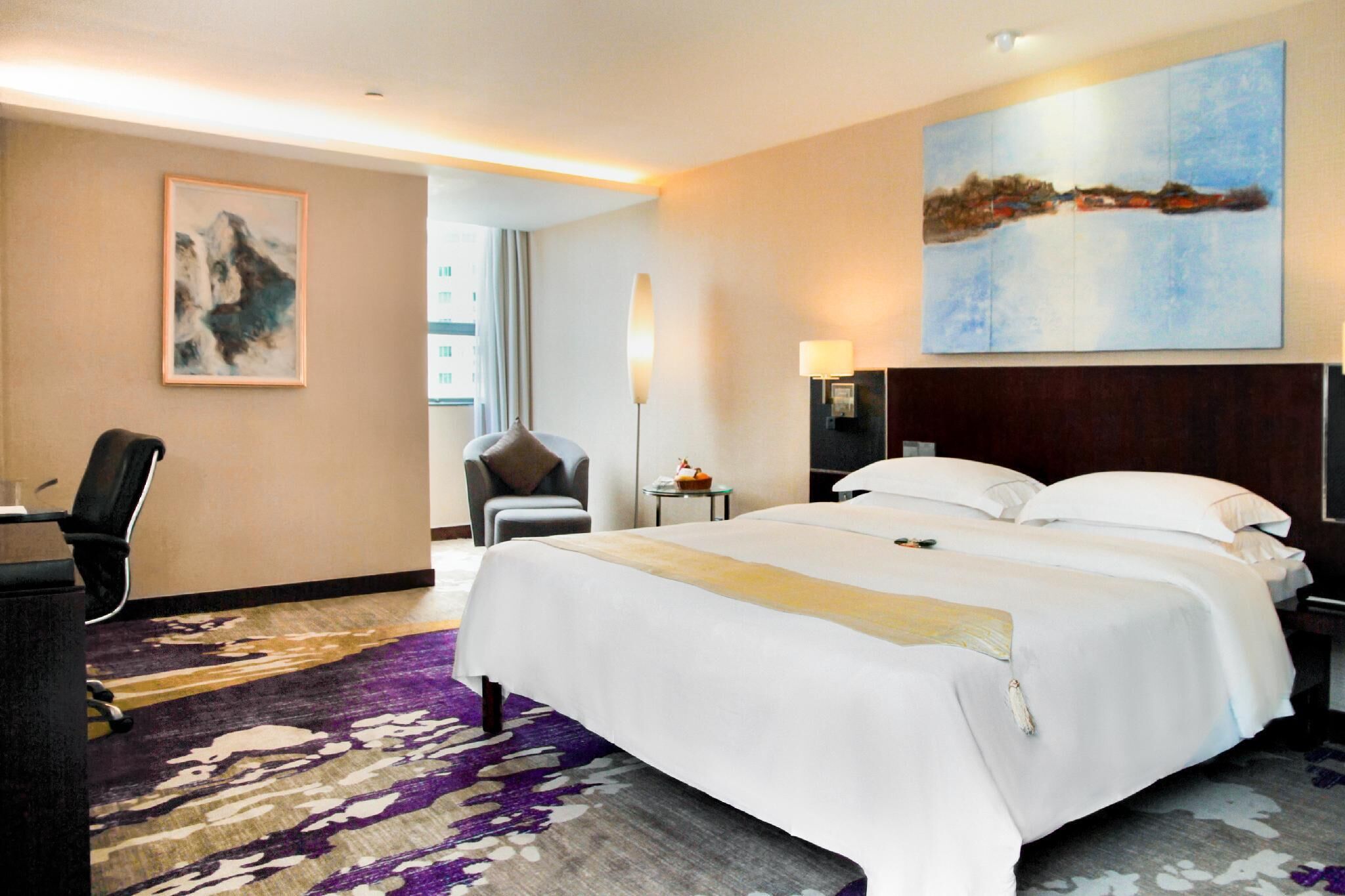 Una habitación de hotel con una cama grande, un escritorio, una silla, una lámpara y un cuadro en la pared.