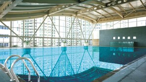 An indoor swimming pool with clear glass walls, metal railings, and a view of high-rise buildings. - The Pavilion Century Tower Hotel (Shenzhen)