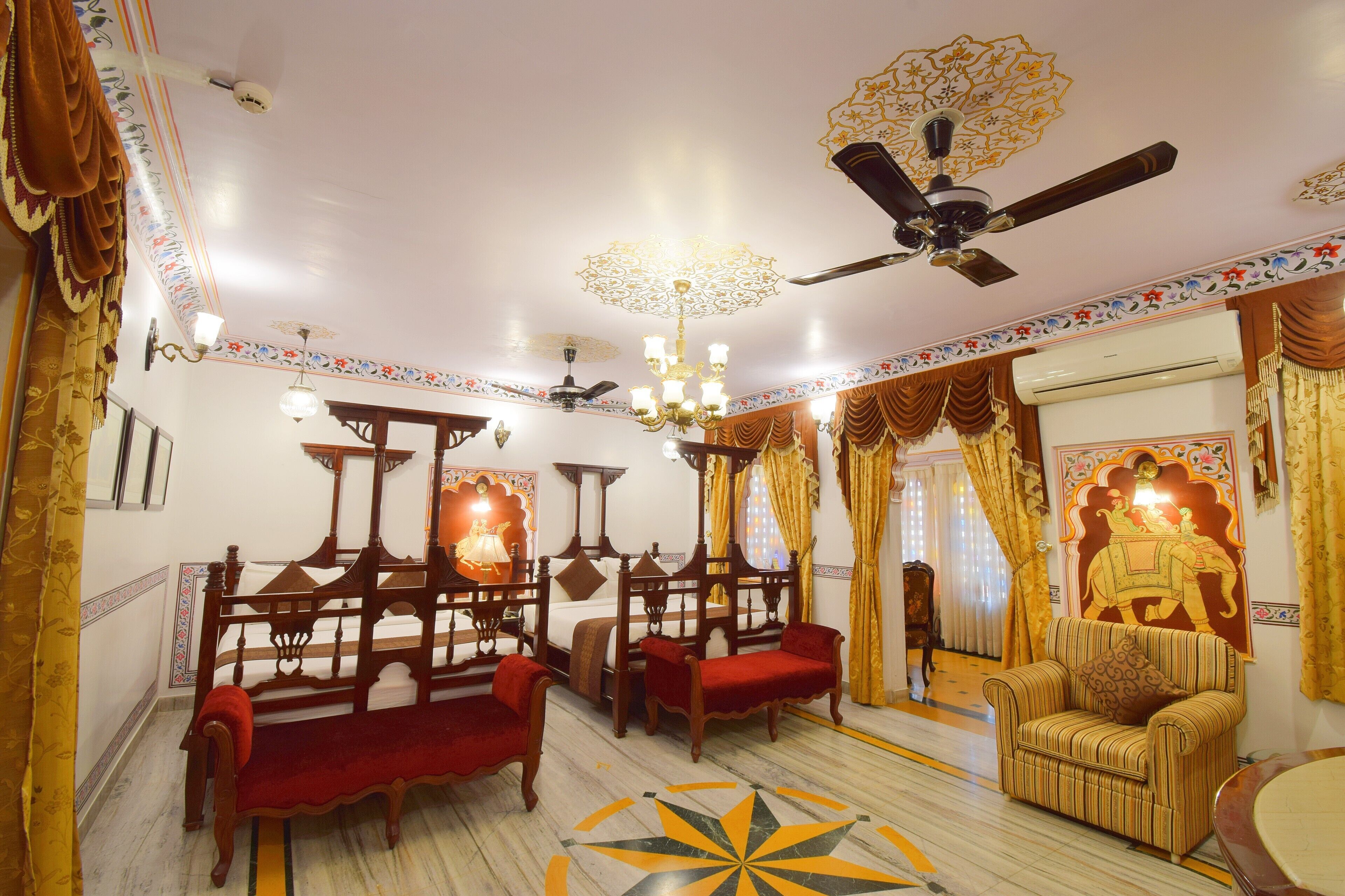 Une chambre de style traditionnel, comprenant un lit, deux chaises en bois, un canapé, un ventilateur de plafond et un lustre décoratif.