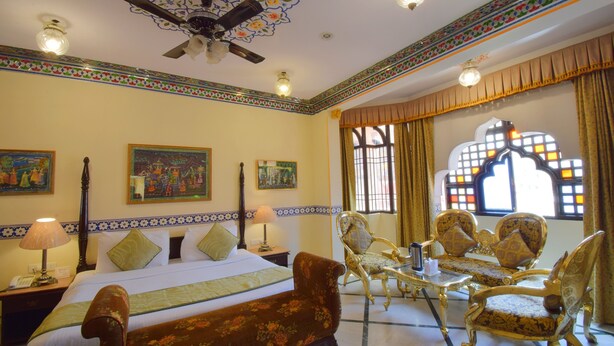 A hotel room with a bed, two chairs, a table, and a decorative window.