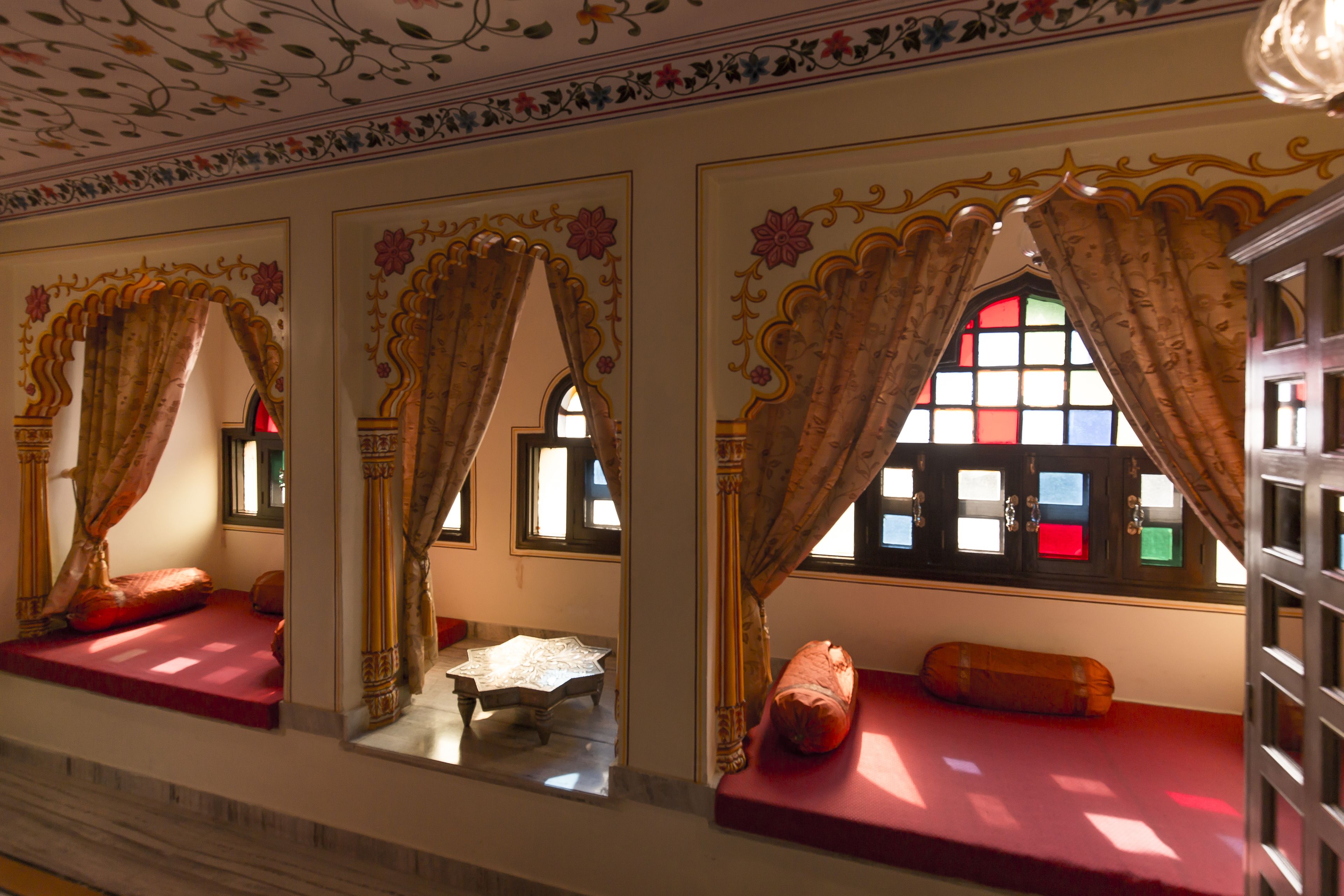 A room with ornate curtains, a red cushioned bench, and a small table with a white cloth.