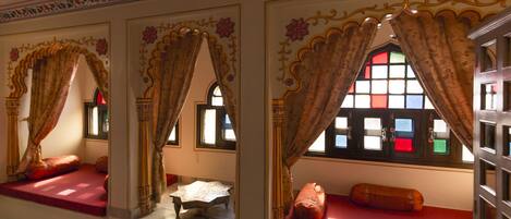 A room with ornate curtains, a red cushioned bench, and a small table with a white cloth.