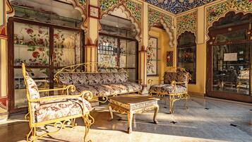 A traditional room with ornate furniture, including a sofa and armchairs, and a decorative glass cabinet.