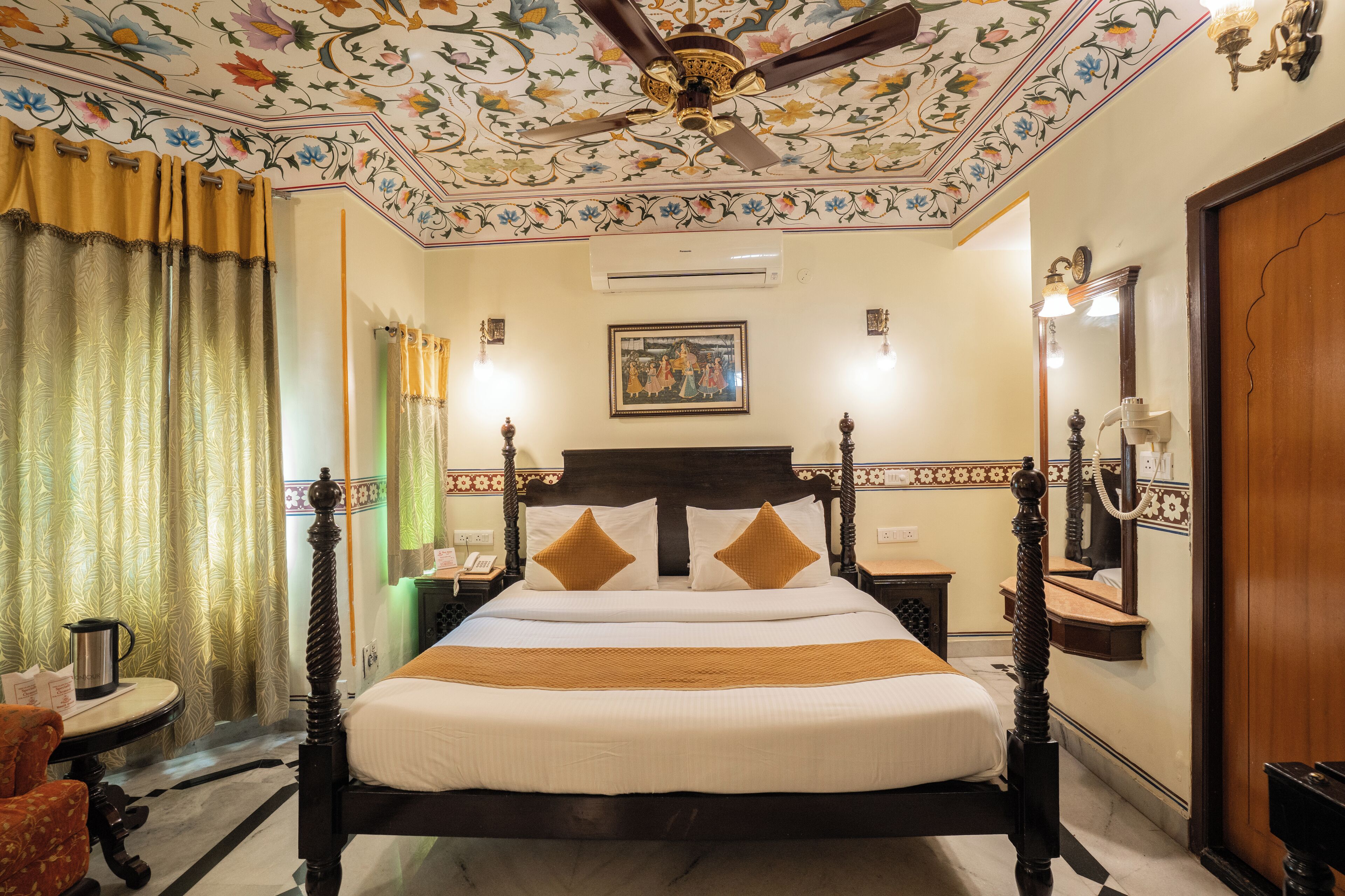 A neatly made bed with a wooden headboard, a ceiling fan, and a floral-patterned ceiling.