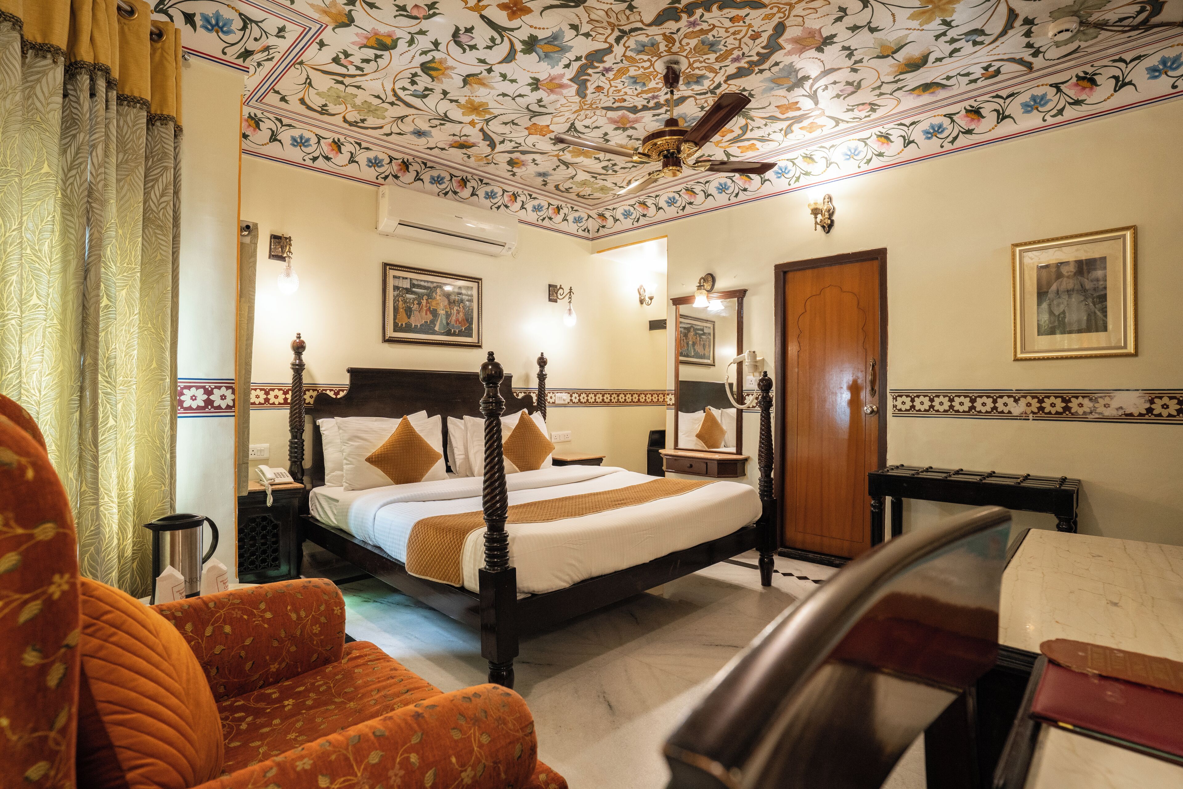 Une chambre d’hôtel avec un grand lit, une tête de lit en bois, un ventilateur de plafond, une table de chevet, une lampe et un miroir.