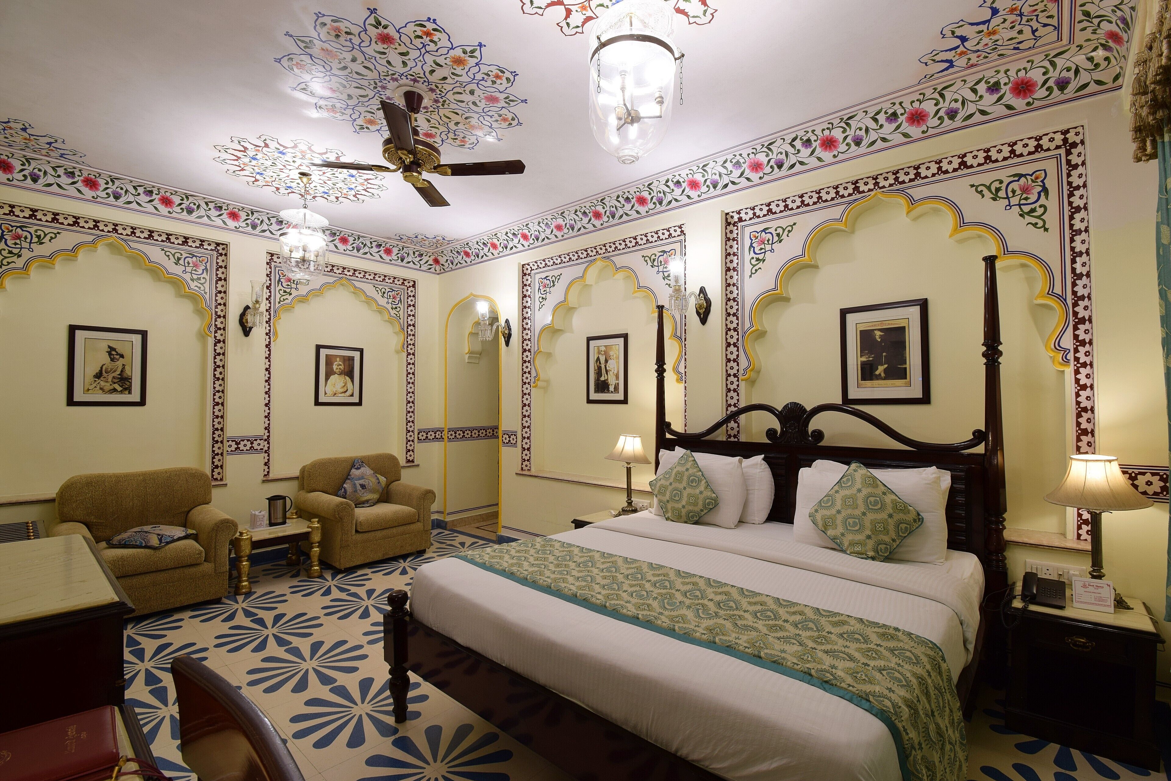 A room with a bed, two armchairs, a desk, and a ceiling fan.