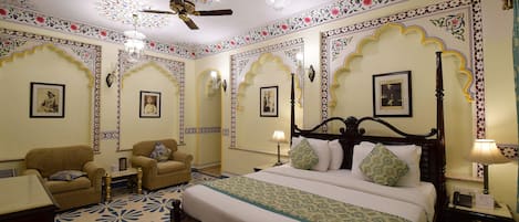 A room with a bed, two armchairs, a desk, and a ceiling fan.