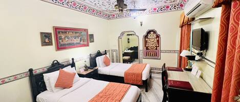 A hotel room with two beds, a desk, a chair, a mirror, and a ceiling with floral patterns.