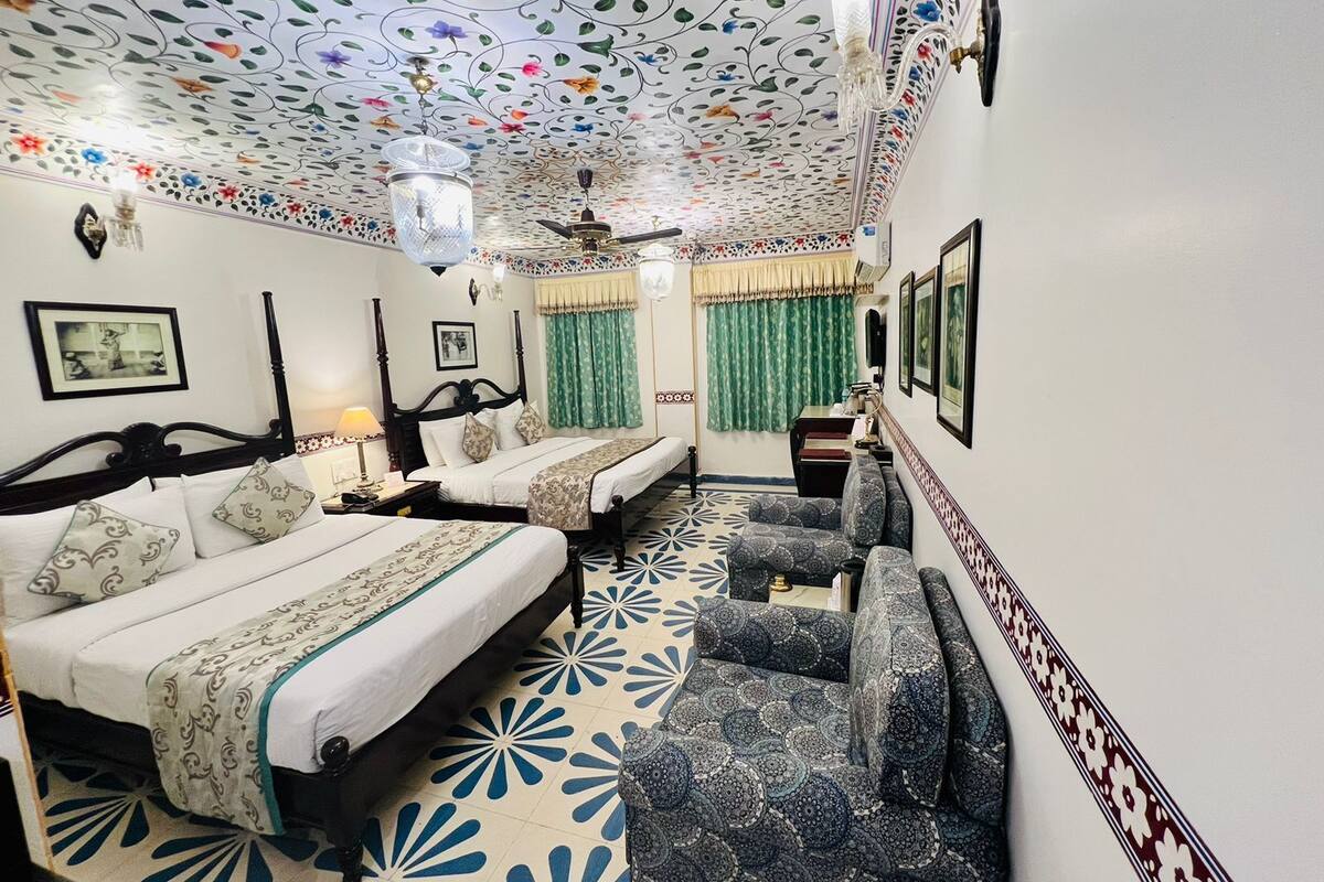 Une chambre avec deux lits, un canapé, une moquette à motifs et un plafond orné de motifs floraux.
