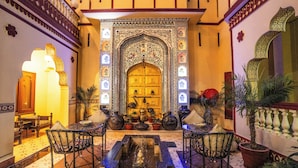 A traditional interior with a central fountain, ornate door, and seating area. - Umaid Bhawan - A Heritage Style Boutique Hotel (Jaipur)