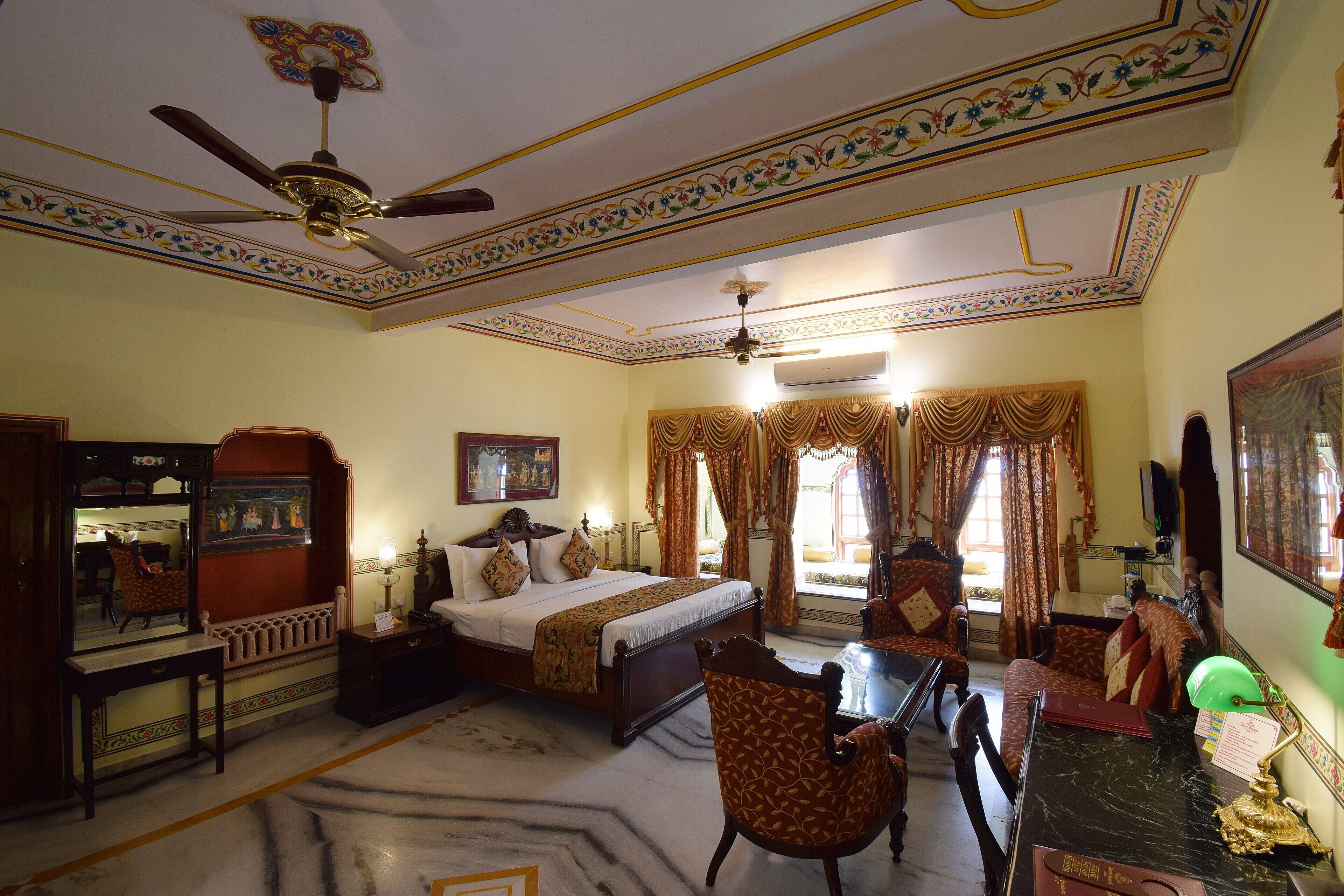 A traditional room with a bed, a desk, a chair, and a ceiling fan.