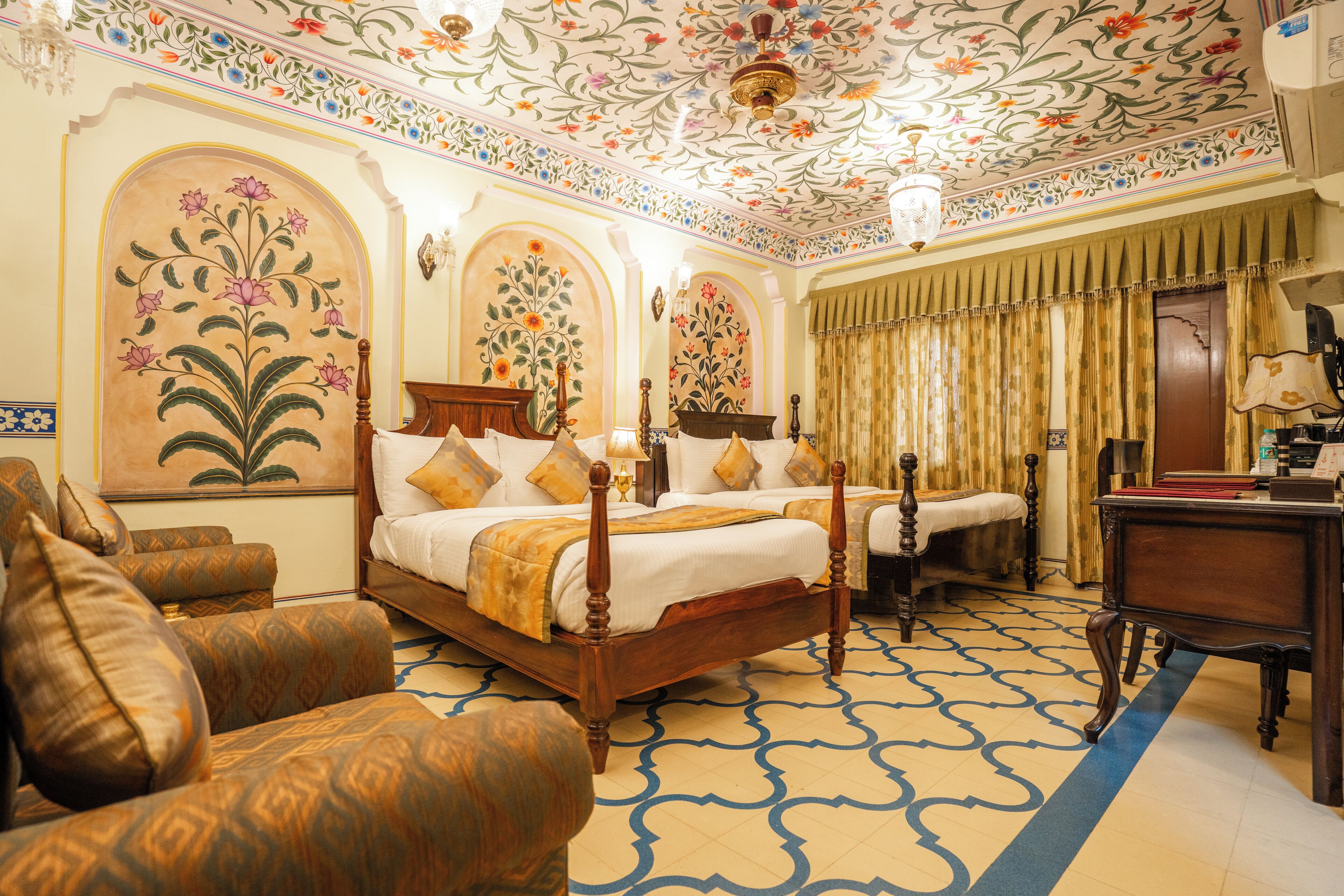 A traditional room with a four-poster bed, a desk, and a patterned carpet.