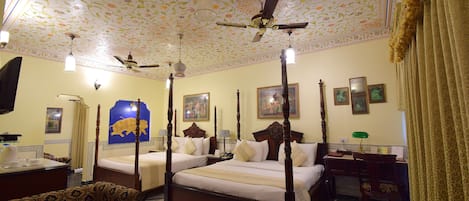 Una cama con dosel y cuatro columnas, un escritorio con silla, un televisor y un techo decorativo.