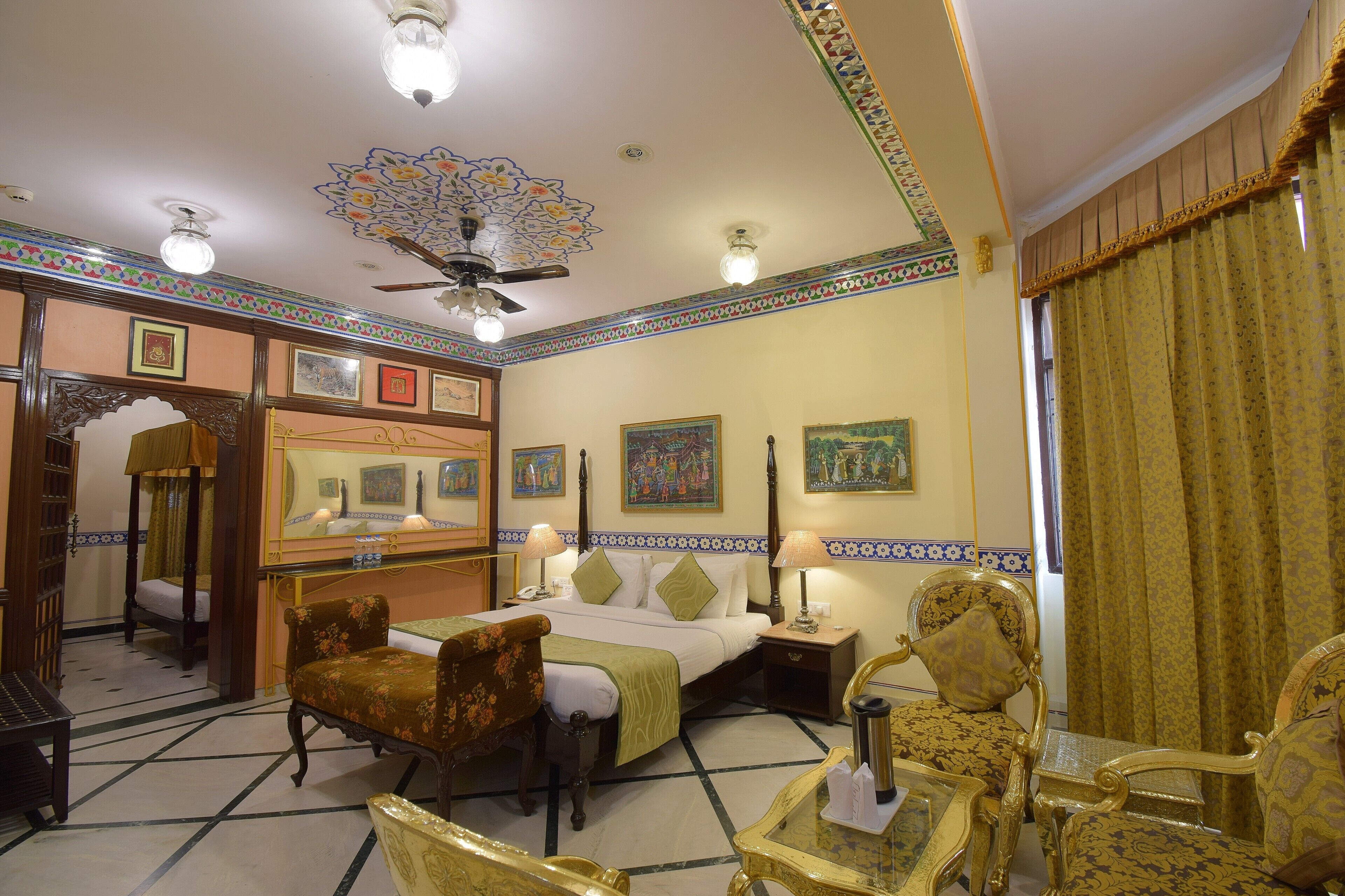 A traditional room with a bed, two chairs, a table, and a ceiling fan.