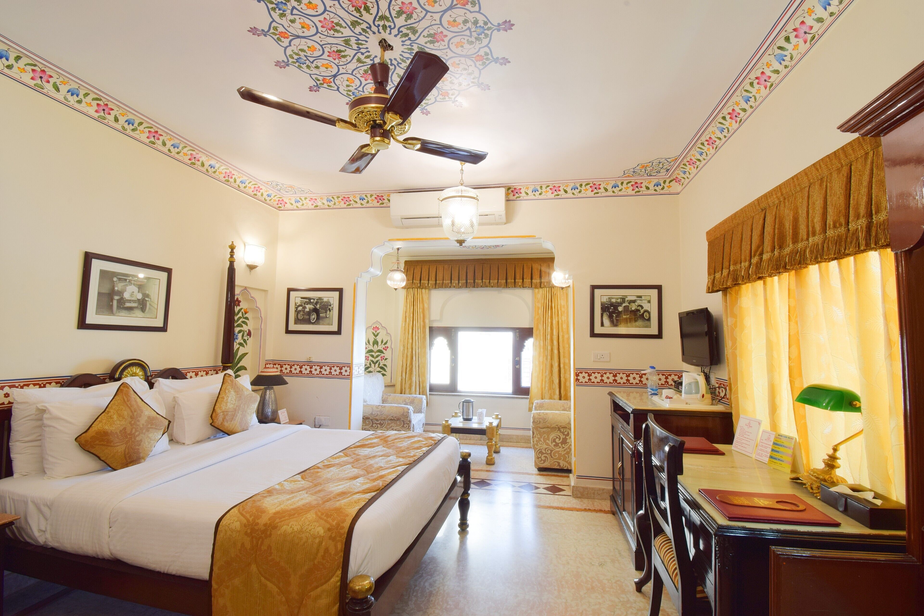 Habitación de hotel con una cama grande, un escritorio con silla, un ventilador de techo y diseños decorativos en las paredes.