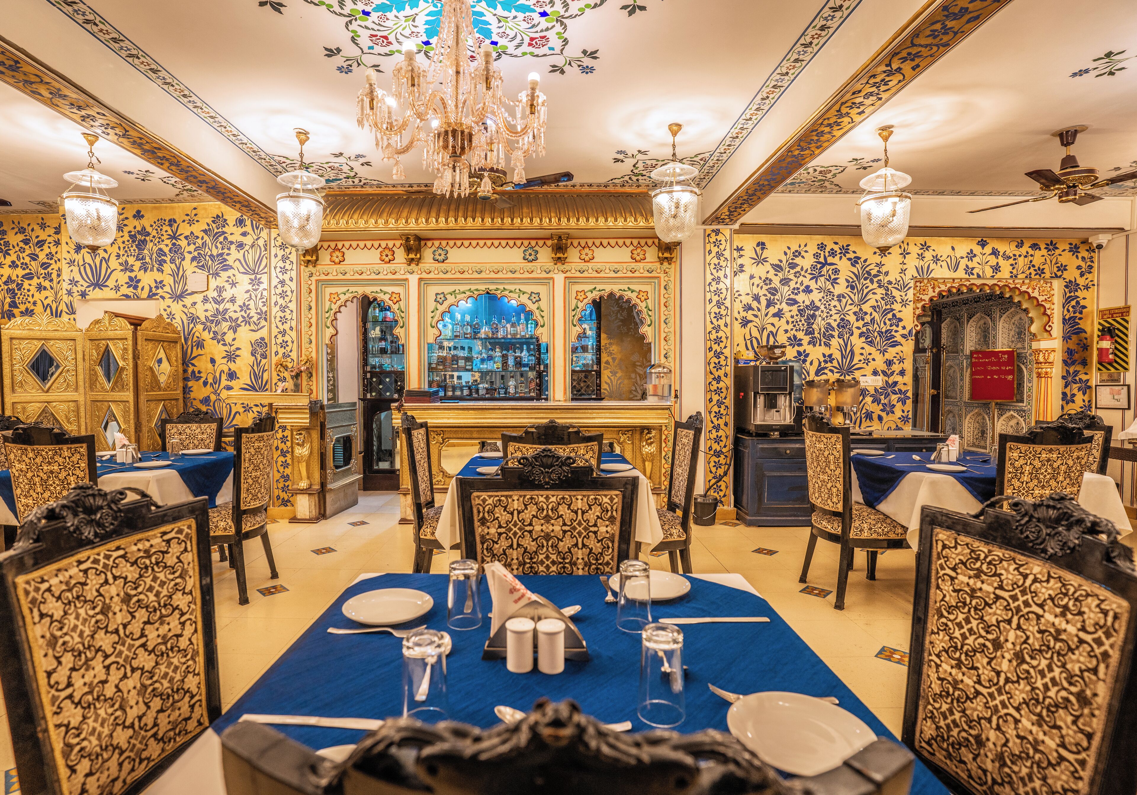 A dining area with ornate decor, chandeliers, and a bar in the background.