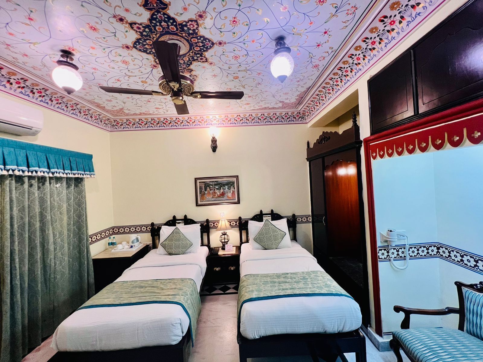 A room with two beds, a ceiling fan, a decorative ceiling, and a framed picture on the wall.