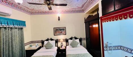 A room with two beds, a ceiling fan, a decorative ceiling, and a framed picture on the wall.