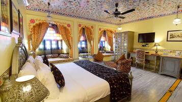 A hotel room with a large bed, a desk, a television, and a ceiling fan.