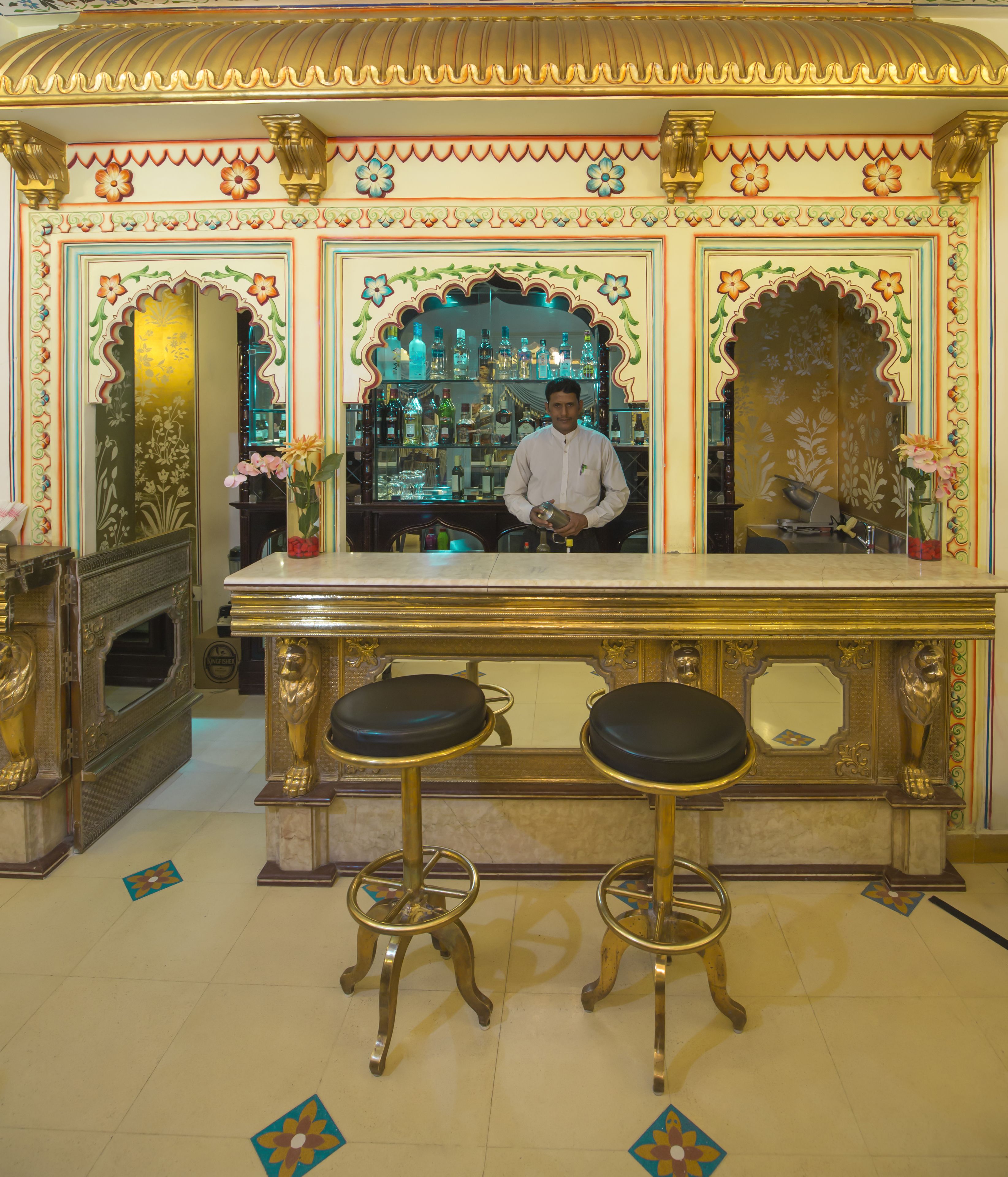 A bar area with ornate decorations, two stools, and a bartender.