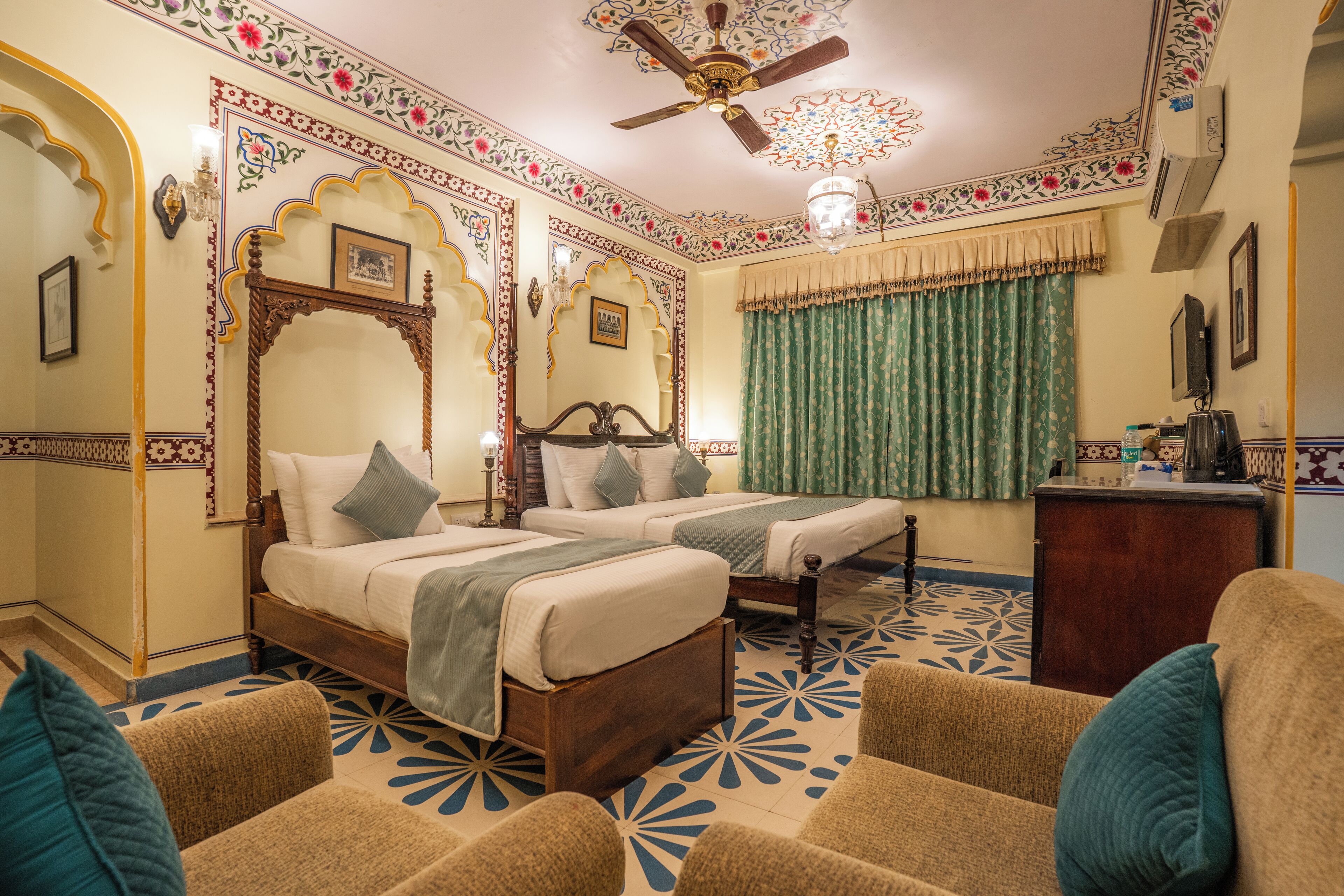 A traditional room with two beds, a ceiling fan, and patterned floor tiles.