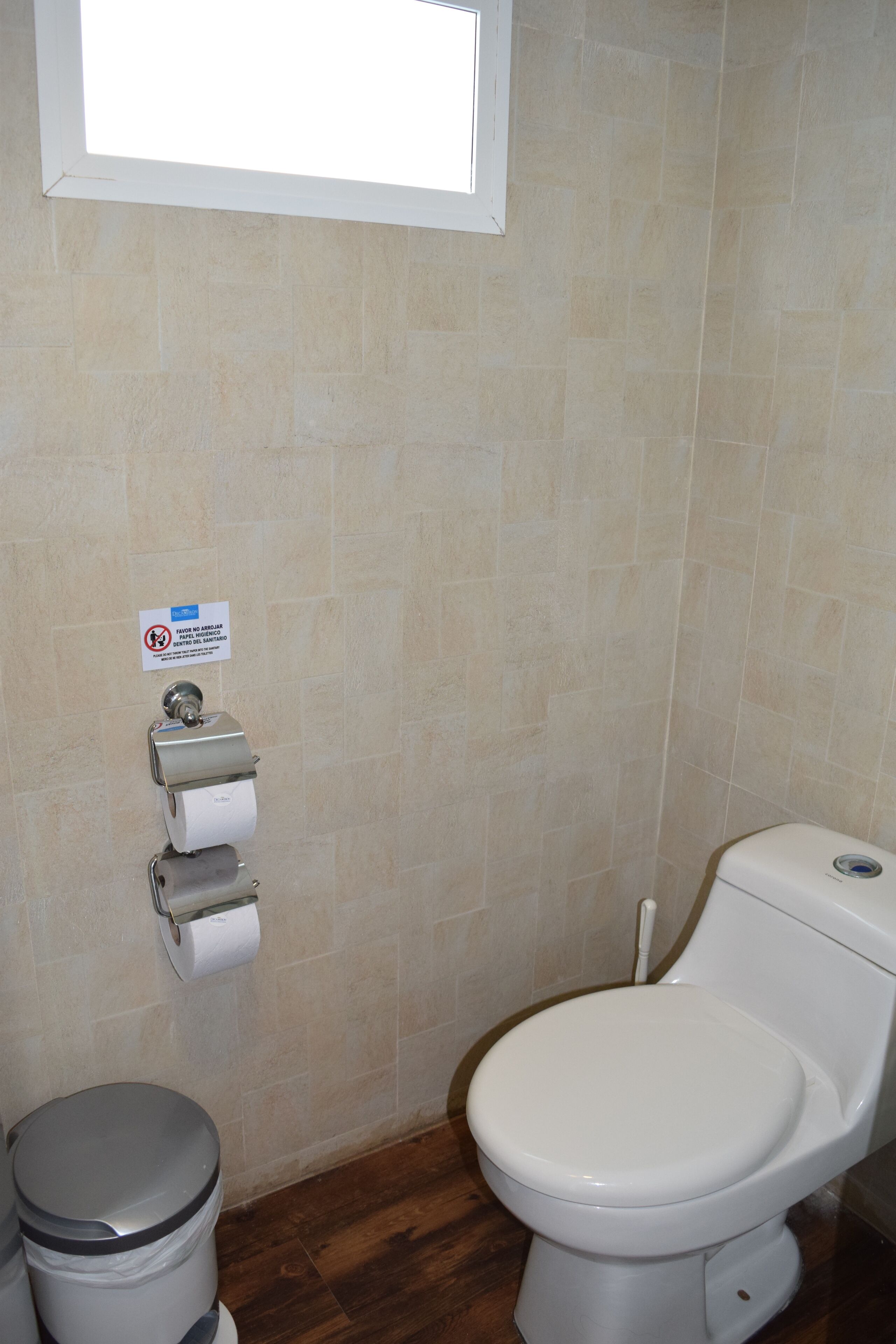 Un baño con inodoro, un cubo de basura y dispensador de toallas de papel.