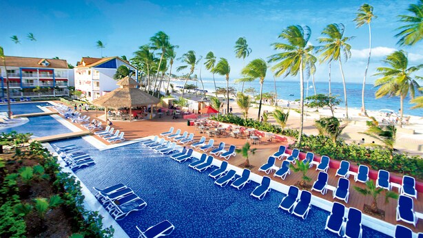 A resort with a swimming pool, beach area, and palm trees.