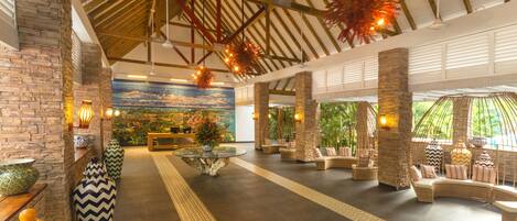 A spacious lobby with a high ceiling, stone pillars, and a central seating area with sofas and a coffee table.