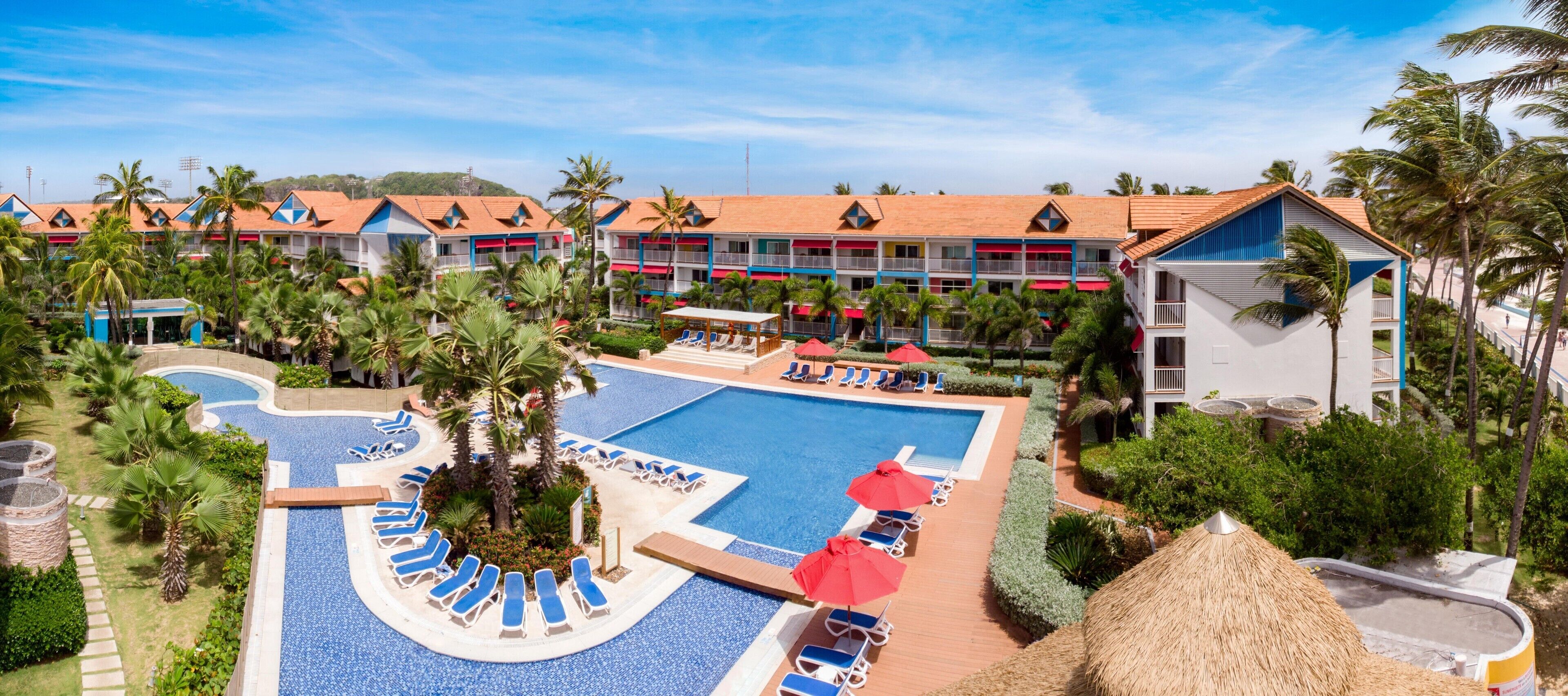 A resort with a central swimming pool surrounded by lounge chairs and palm trees.