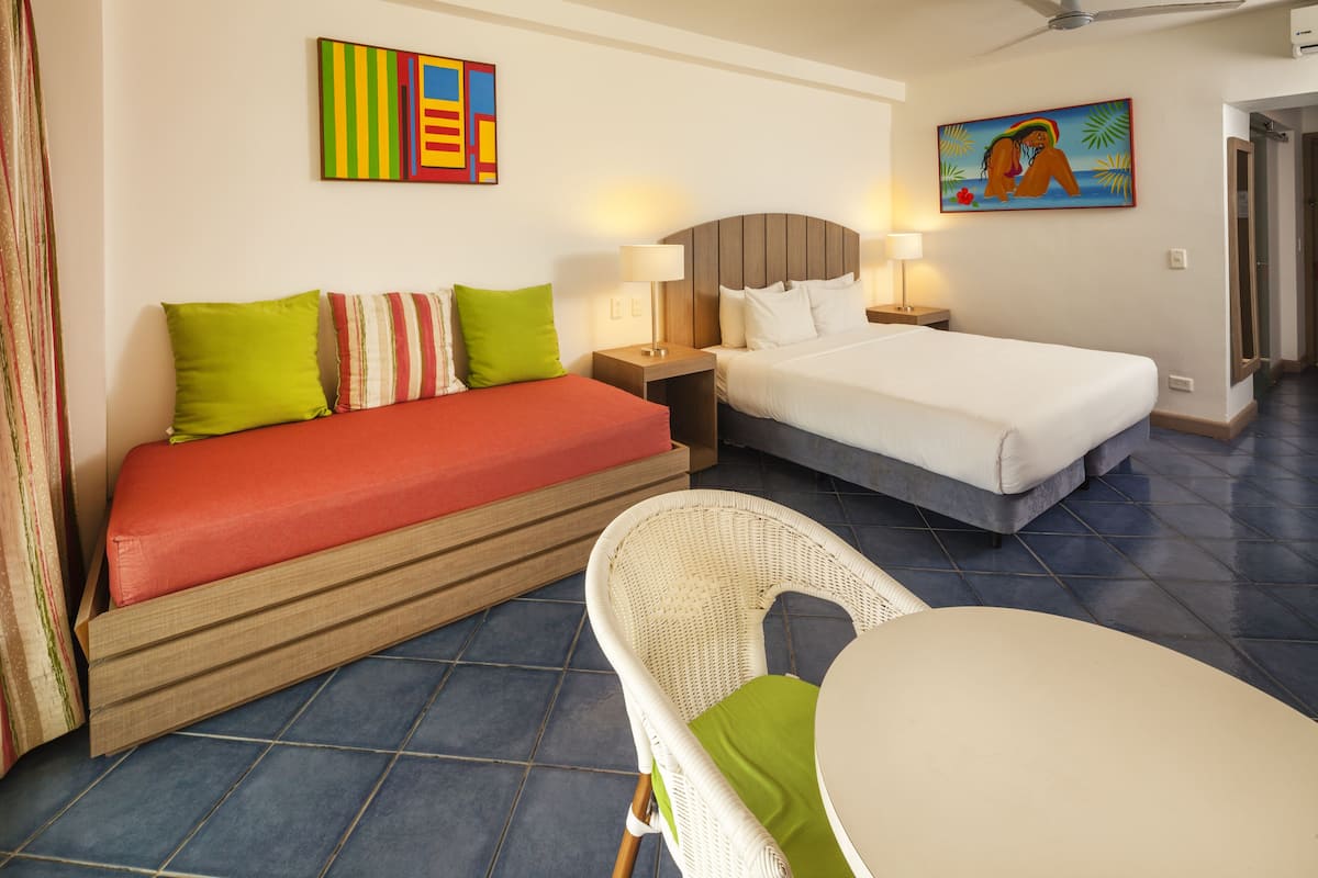 A hotel room with a large bed, a smaller bed, a wicker chair, and a small table.