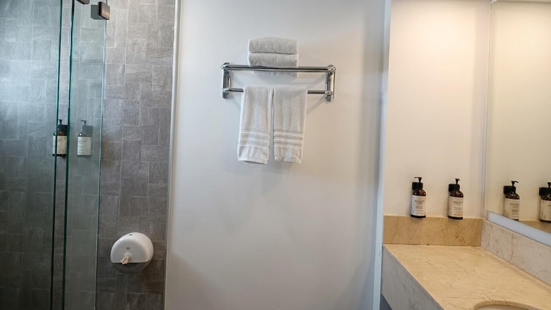 Un baño con cabina de ducha de vidrio, un perchero con dos toallas y una encimera con artículos de aseo.