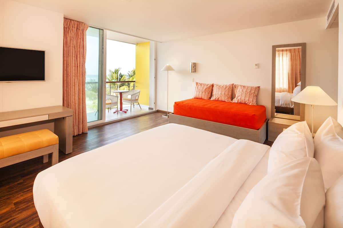 A hotel room with a large bed, a desk, a chair, and a balcony with a table and chairs.