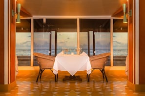 A dining area with a table and chairs facing a large window overlooking the sea. - Decameron San Luis - All Inclusive (San Andrés)
