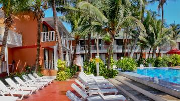 A hotel with a swimming pool, lounge chairs, and palm trees.