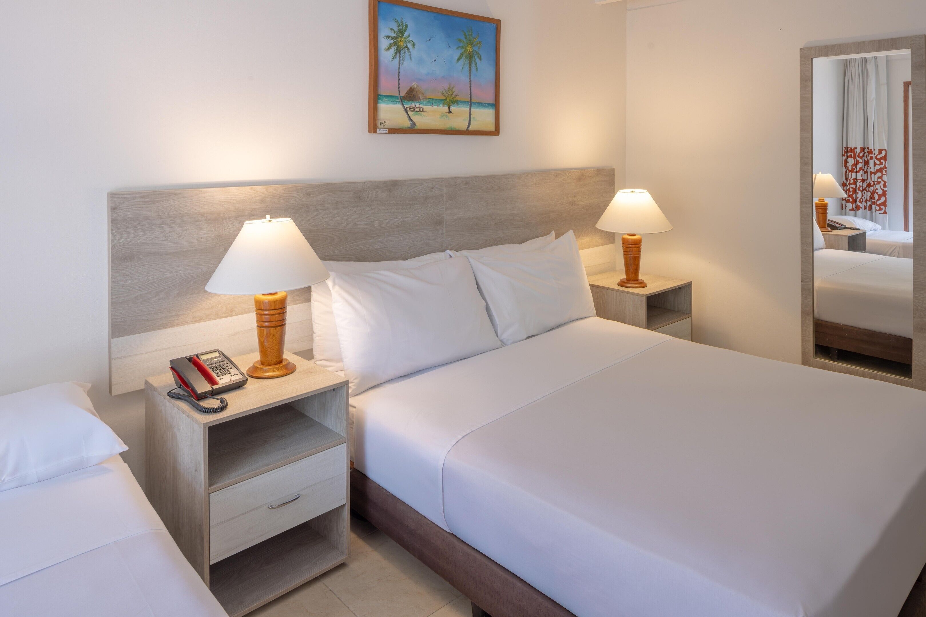 A hotel room with a large bed, two bedside tables with lamps, a telephone, and a painting of a beach scene.