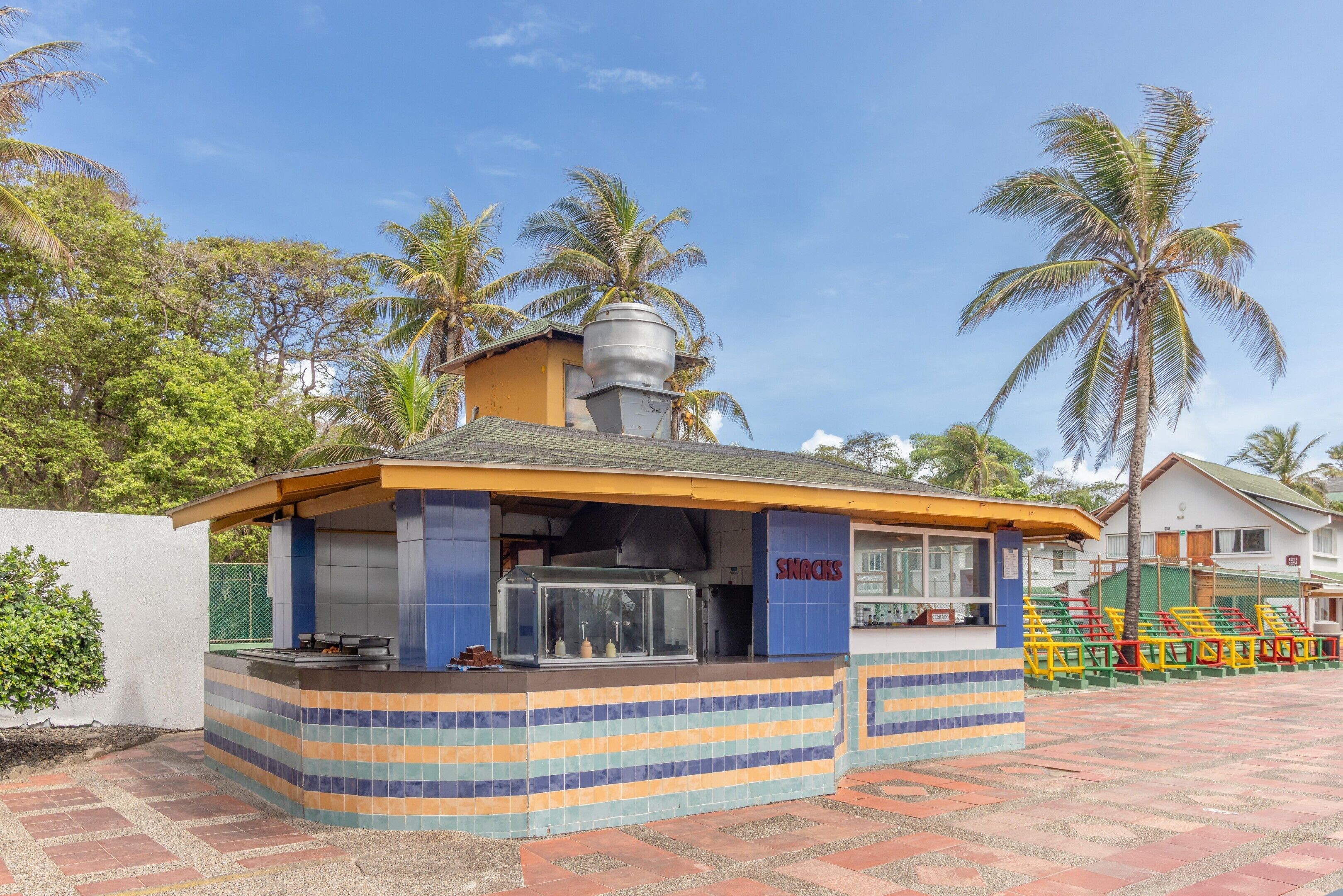 Un pequeño kiosco al aire libre con mostrador de azulejos y un letrero que dice 'SNACKS'.