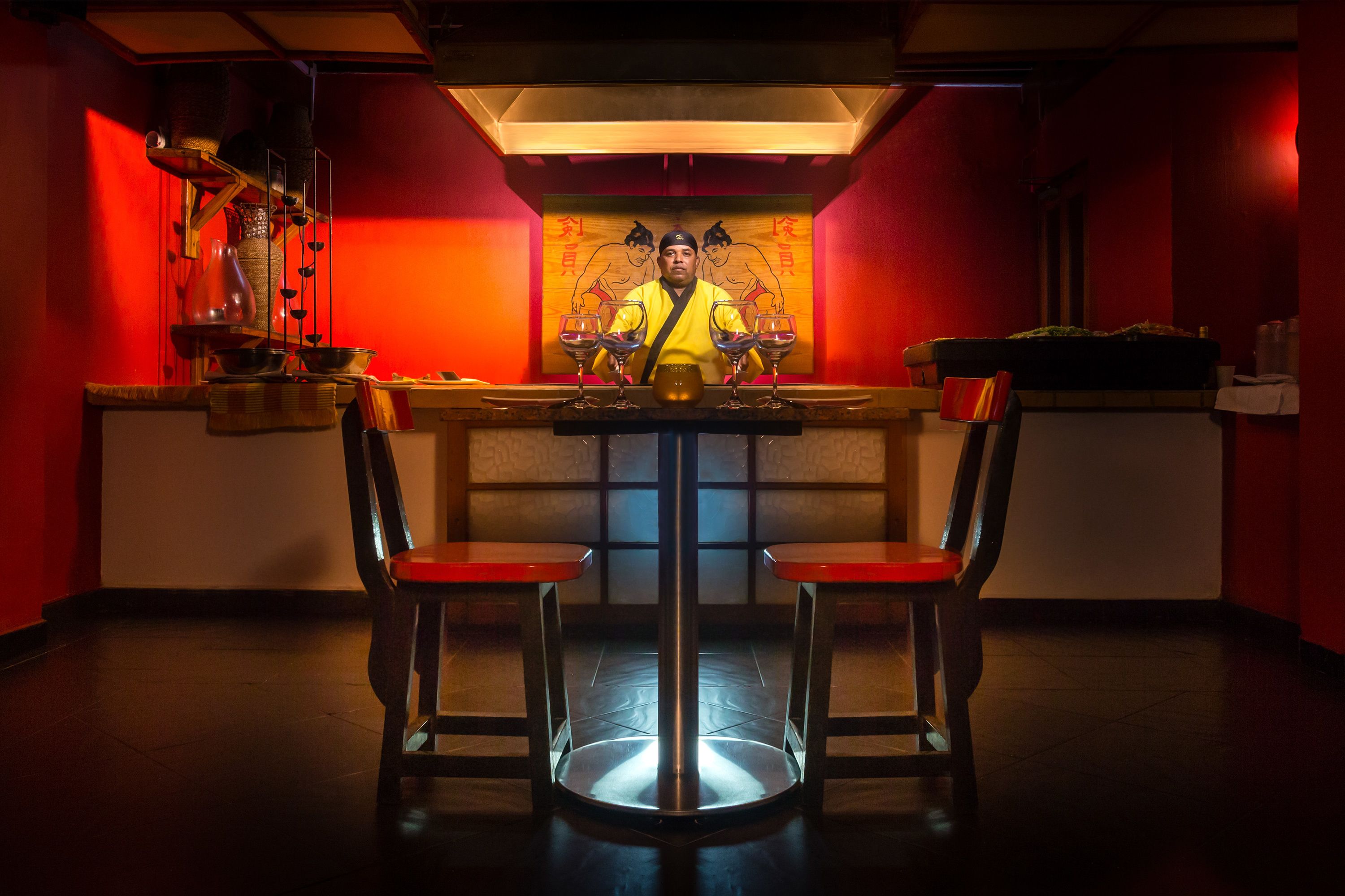 Ein Restaurantinneres mit einem Tisch in der Mitte, zwei Stühlen und einer Person, die hinter dem Tisch steht.
