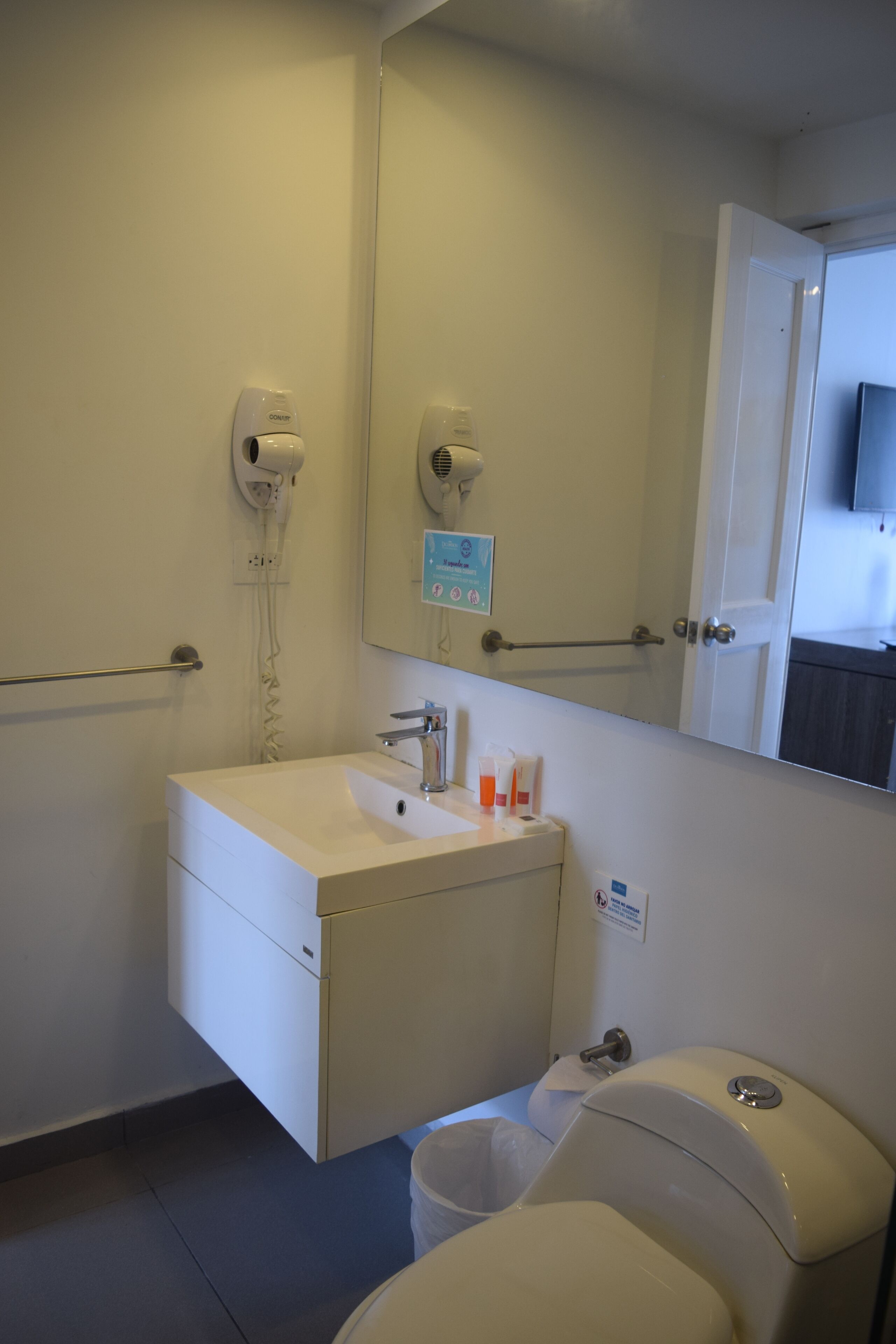 A bathroom with a white sink, a mirror, a hand dryer, and a toilet.