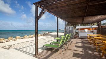 A beachside patio with wooden deck, lounge chairs, and tables.
