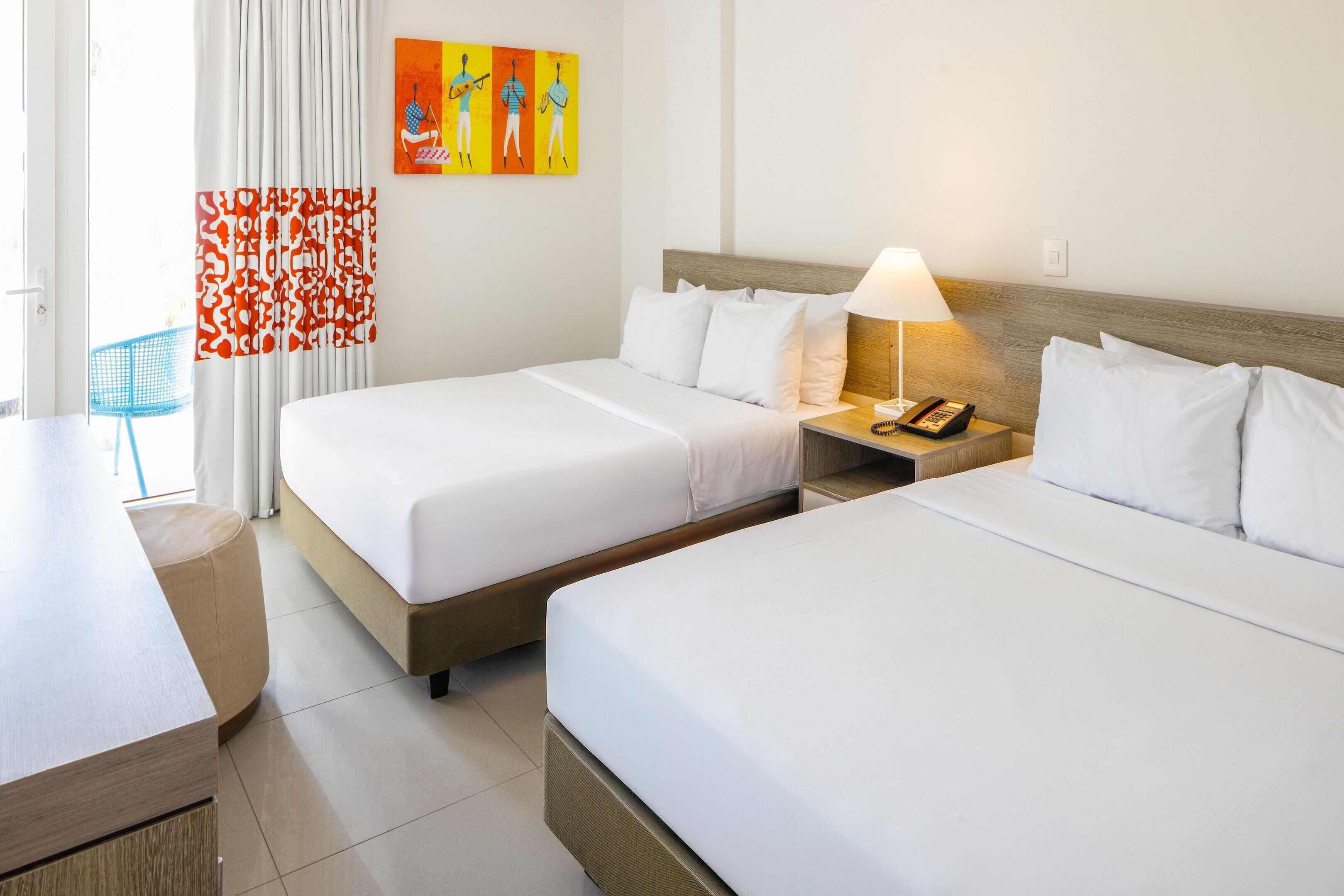 Una habitación de hotel con dos camas individuales, una mesita de noche con una lámpara, un teléfono y una obra de arte colgada en la pared.